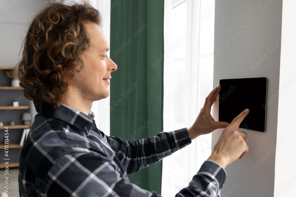 Aufkleber Man Using Tablet On Wall With Smart Home Application Indoors
