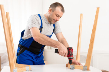 Repairman In Blue Uniform Fixing Table With Electric Drill Indoors