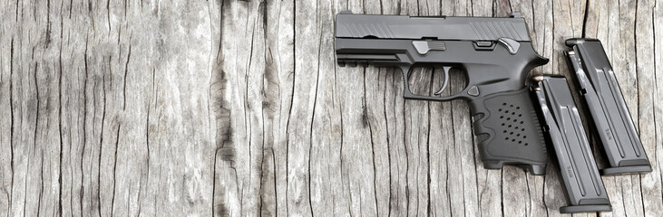 Black automatic 9mm pistol and magazines on wooden floor, soft and selective focus on pistol,...