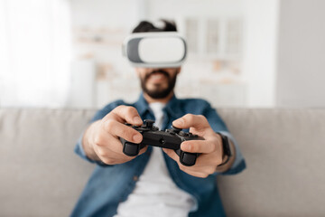 Enjoying virtual reality glasses, 3d spectacles and controller gamepad at home. Young arab man playing computer games