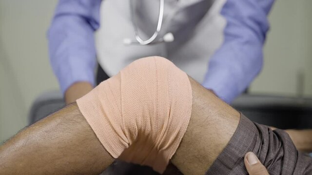 Close up of Unrecognizable doctor unwrapping stretch bandage after recovering from knee sprain or joint paint from patient - concept of knee sprain and muscle injury treatment.