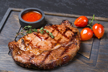 fried Rib Eye steak with cherry tomatoes and sauce on a wooden board.