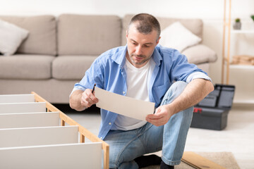 Man Reading Furniture Assembly Manual Installing Wooden Shelf At Home