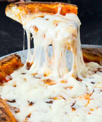 Tasty take slice of pizza with cheese. Appetizing separate piece of round pizza stretching melted cheese.