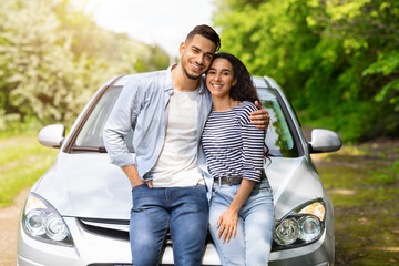 Loving arab man and woman sitting on auto hood, hugging