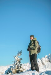 Fototapeta na wymiar Man hiker with backpack trekking in mountains. Winter sport activity snow mountain hills. Winter hiking cold weather with backpack on snow trail forest in Carpathian evergreen coniferous trees