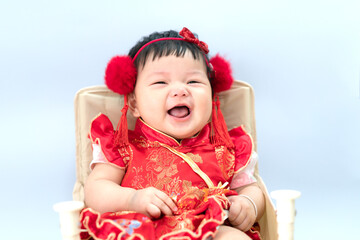 Happy cute infant baby girl in Chinese dress sitting in white living room. Cute Asian infant baby sitting in a white living room as concept of Chinese New Year.