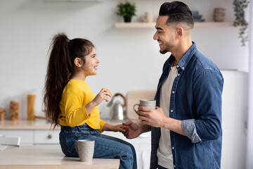 Cute Little Girl And Her Arab Dad Having Snacks In Kitchen Together