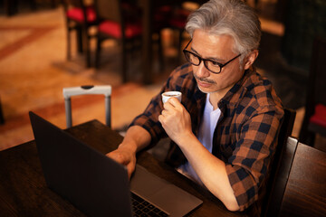 Businessman working on laptop in cafe. Handsome senior man enjoying in fresh coffee