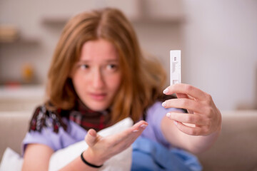 Young sick woman holding pregnancy test at home