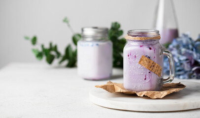 Milk black currant smoothie in a glass jar decorated with flowers on a table. Healthy milkshake beverage.