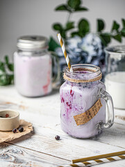 Milk black currant smoothie in a glass jar decorated with flowers on a table. Healthy milkshake beverage.
