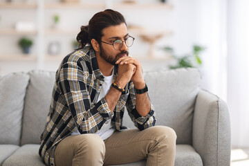 Pensive arab guy sitting on couch at home