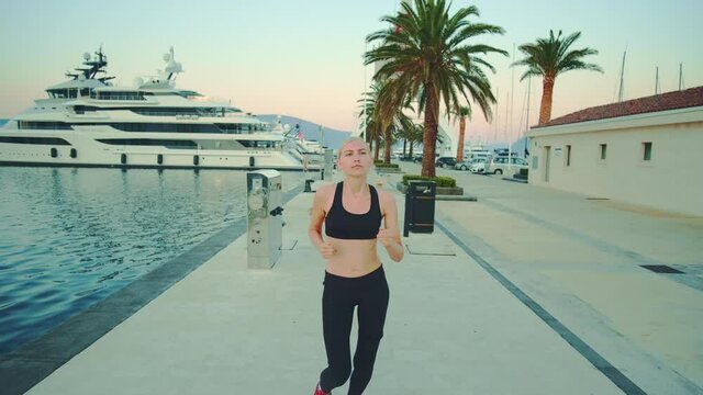 Fit woman jogging in the morning in the sea port. In the background there are palm trees and yachts