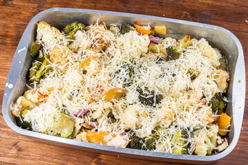 Cooking baked vegetables with cheese - vegetables, broccoli and cauliflower in a baking sheet sprinkled with grated cheese, close-up