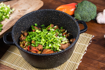Cooking chicken stews - vegetables with chicken in a saucepan on a table with ingredients nearby