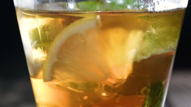 Closeup glass of iced tea with ice cubes, sliced lemon, fresh pepermint. Healthy refreshing lemonade for detoxification, sweet tasty soft drink or cold aromatic beverage for summer time in slow motion