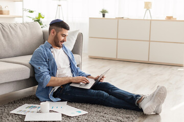 Cheerful male jew working on laptop at home on floor