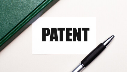 On a light gray background lies a pen, a green notebook and a white card with the text PATENT. Business concept.