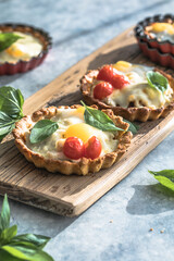 Savory mini pie (quiche) with chicken, bacon, tomato and  egg decorated by leaf of basil on grey background.