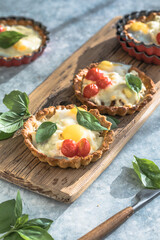 Savory mini pie (quiche) with chicken, bacon, tomato and  egg decorated by leaf of basil on grey background.