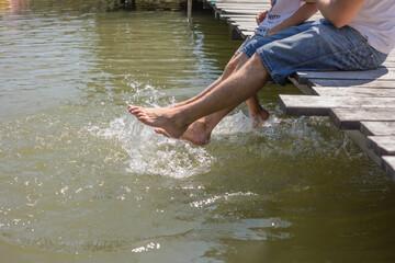 Legs of barefoot friends splashing water in lake while enjoying summer rest