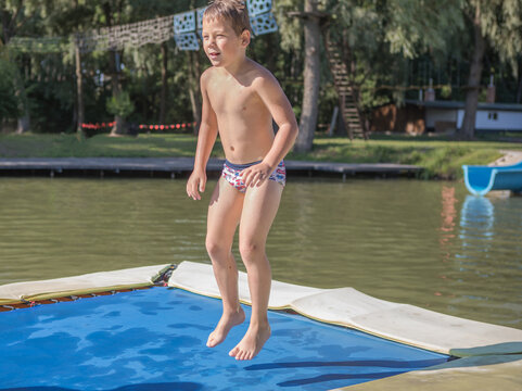 boy jumping from a trampoline into the pool. Children jump on inflatable water slide. Aqua amusement park in exotic island resort.