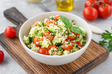 Tabbouleh salad. Couscous salad with fresh vegetables and herbs in a bowl on a gray concrete...