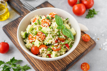 Tabbouleh salad. Couscous salad with fresh vegetables and herbs in a bowl on a gray concrete background. Copy space.