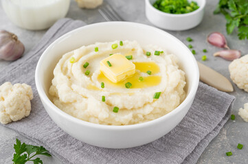 Cauliflower puree with butter and green onions in a white bowl on a gray concrete background. Healthy food. Copy space.