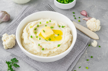 Cauliflower puree with butter and green onions in a white bowl on a gray concrete background. Healthy food. Copy space.