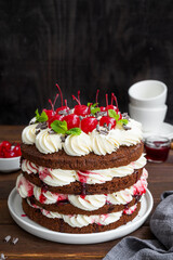 Naked Black forest cake, Schwarzwald pie. Cake with dark chocolate, whipped cream and cherry on a dark wooden background. Copy space.