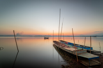 Naklejka na ściany i meble Two small boats moored on the shore of the lake. at sunset beautiful light