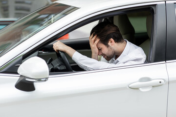 Businessman sitting in own car stuck in traffic, holding his hand on forehead and nervously waiting