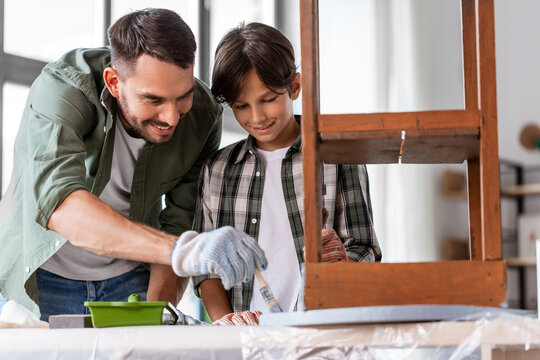 renovation, diy and home improvement concept - father and son in gloves with paint brush painting old wooden table in grey color at home
