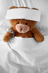 medicine, healthcare and childhood concept - ill teddy bear toy with cooling head bandage and...