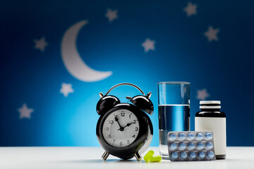 sleep disorder, bedtime and medicine concept - close up of alarm clock, glass of water, earplugs and sleeping pills over moon and night stars on blue background - obrazy, fototapety, plakaty