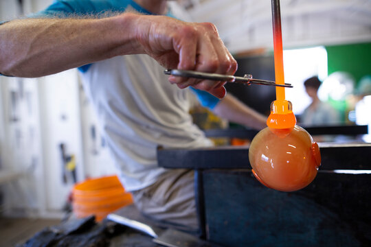 Glassblower clipping molten glass with scissors in workshop