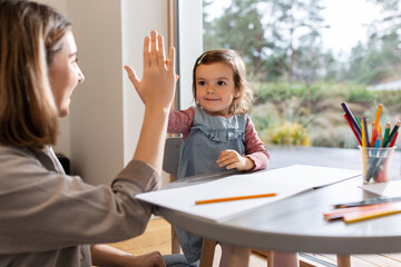 family, motherhood and leisure concept - mother spending time with her little daughter and making high five gesture at home