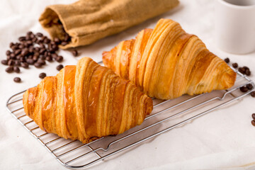 2 croissants are placed on a wire rack and coffee beans are poured from sacks scattered on the floor, breakfast, snacks or bakery.
