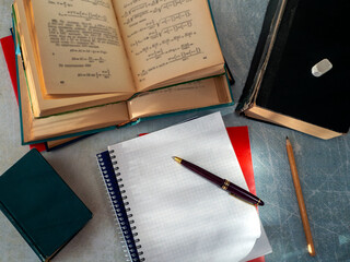 Open and closed notebooks and textbooks lie on the table. There is a pen on a blank sheet of...