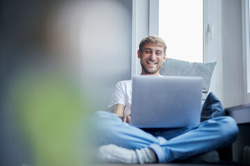 Smiling businessman using laptop sitting on sofa at home