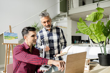 Businessman holding wind turbine model pointing at laptop to colleague