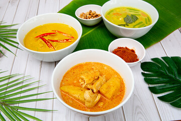 Red, green and massaman curries on a white background with two green leaves and some curry paste and peanuts