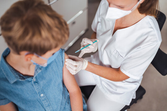 Nurse in protective face mask administering boy with COVID-19 vaccine