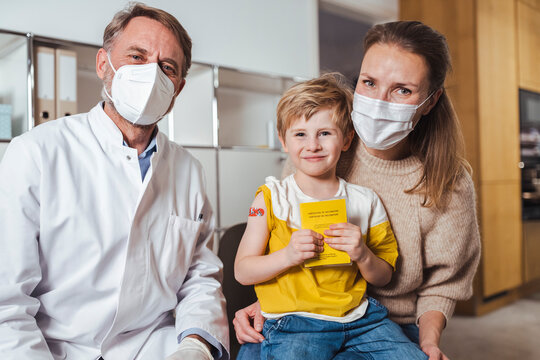 Smiling boy holding vaccination certificate with doctor and mother at center