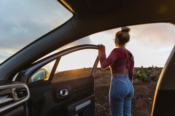 Woman standing by open car door at sunset