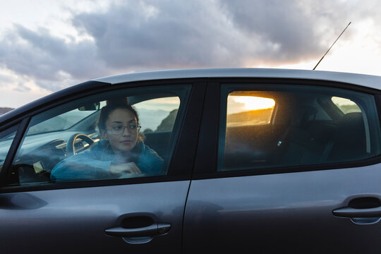 Young woman looking out through car window at sunset