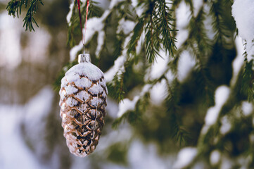 Close-up of a Christmas tree toy in shape of cone hanging on a branch in a snowy forest. Winter...