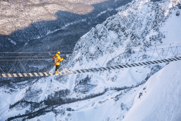 Man hiking over snowcapped mountain on rope bridge